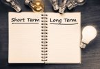 Short term and Long term on opened notebook with glowing light bulb